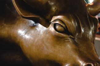 Close-up of the bronze Charging Bull statue, focusing on its eye, ear, and part of its face, with polished metal reflecting the surrounding light.